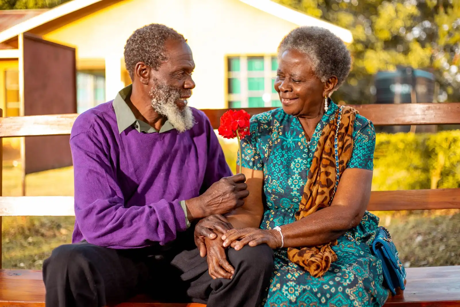 Older couple smiling at each other on a bench outside their home